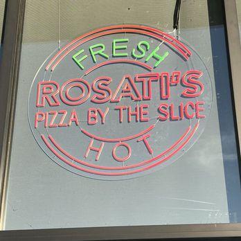 Rosati's Pizza - Neon sign displayed in a window for Rosati's Pizza by the Slice, with the words 'Fresh' in green at the top, 'Rosati's' in large red letters in the center, 'Pizza by the Slice' below, and 'Hot' in red at the bottom. The sign is illuminated and mounted on a glass window, with visible wiring at the top. - Pizza Near Me - Orem, Utah