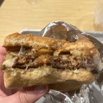 Hello Bistro - Build Your Own Burger- Beyond Burger - A burger with melted cheese and meat is held in a hand, partially eaten, with aluminum foil wrapping. The background shows a wooden table and some food trays. - Salad Near Me - Pittsburgh, Pennsylvania
