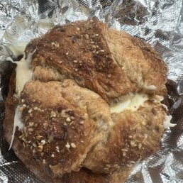 Sausage egg and cheese on a delicious croissant - Four baked chicken thighs with a golden-brown exterior, topped with melted cheese and sprinkled with seasoning and chopped nuts, resting on crinkled aluminum foil. The image shows a close-up of the cooked poultry, highlighting the texture and toppings.