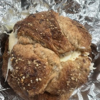 Bearded Baking - Sausage egg and cheese on a delicious croissant - Four baked chicken thighs with a golden-brown exterior, topped with melted cheese and sprinkled with seasoning and chopped nuts, resting on crinkled aluminum foil. The image shows a close-up of the cooked poultry, highlighting the texture and toppings. - Bakeries Near Me - Hampton, New Hampshire