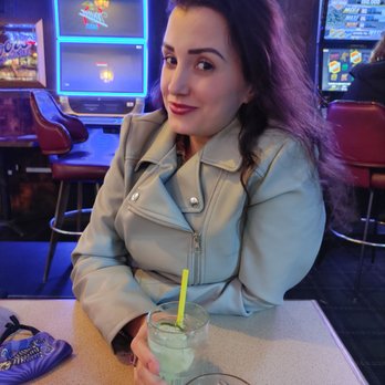 Glass House Tavern - a woman sitting at a table with a drink - Bars Near Me - Portland, Oregon Glass House Tavern - a woman sitting at a table with a drink - Bars Near Me - Portland, Oregon