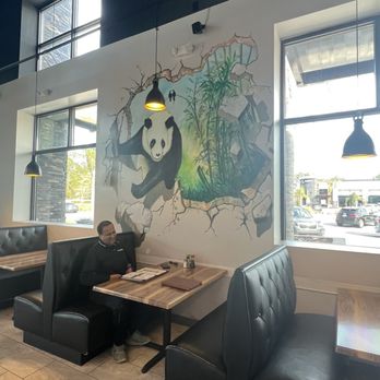 Nori Restaurant - A person is seated in a booth at a restaurant, with a panda mural painted on the wall behind them, and large windows providing natural light. - Asian Fusion Near Me - St. Augustine, Florida
