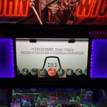 Free Play Bar Arcade - If you are curious the score was 14,200,000 in this mode. Not bad. - The image features a pinball machine screen displaying initials and a message, including the text 'MY50CHEESES Enter Initials' and 'EXCOMMUNICADO MULTIBALL CHAMPION.' The screen is surrounded by purple LED lights, and below it, there is a neon-lit cityscape artwork with tall buildings and bright outlines, indicating an arcade environment. - Bars Near Me - Providence, Rhode Island