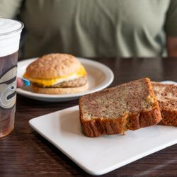 Ziggi's Coffee - Iced coffee with cold foam in a Ziggi's cup with a breakfast sandwich and sliced loaf cake on a table.