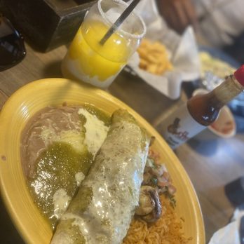 El Nopal - Mexican dish with rice and beans. Mango margarita, chips and salsa - A Mexican meal is served on a yellow plate, including a rolled taco topped with sauce, rice, and beans with green sauce. A mango margarita with a straw and salted rim is placed nearby, with chips and salsa in the background. The setting appears to be a casual restaurant with other dishes and drinks visible. - Mexican Near Me - Dover, Delaware