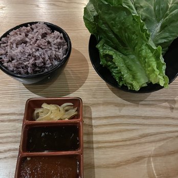 Char'd - Comes with the Galbi - A meal setup includes a bowl of multigrain rice, a bowl of fresh lettuce leaves, and three small dishes with sauces and pickled vegetables on a wooden table. - Korean Near Me - Milwaukee, Wisconsin