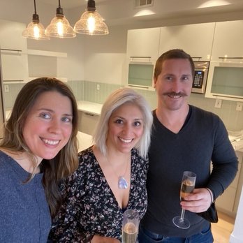 Brick & Mortar - A group of three individuals, two women and one man, are smiling and holding glasses of champagne in a contemporary kitchen setting. - Real Estate Services Near Me - Brooklyn, New York