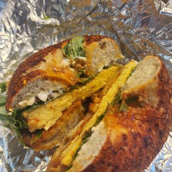 Breadhive Bakery & Cafe - The Nina - A sandwich with fried bread, scrambled eggs, greens, and possibly sausage, wrapped in aluminum foil, partially cut open. - Cafes Near Me - Buffalo, New York