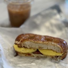 Bacon, egg, and cheese pretzel breakfast sandwich. Cold brew in the background. Bacon, egg, and cheese pretzel breakfast sandwich. Cold brew in the background.