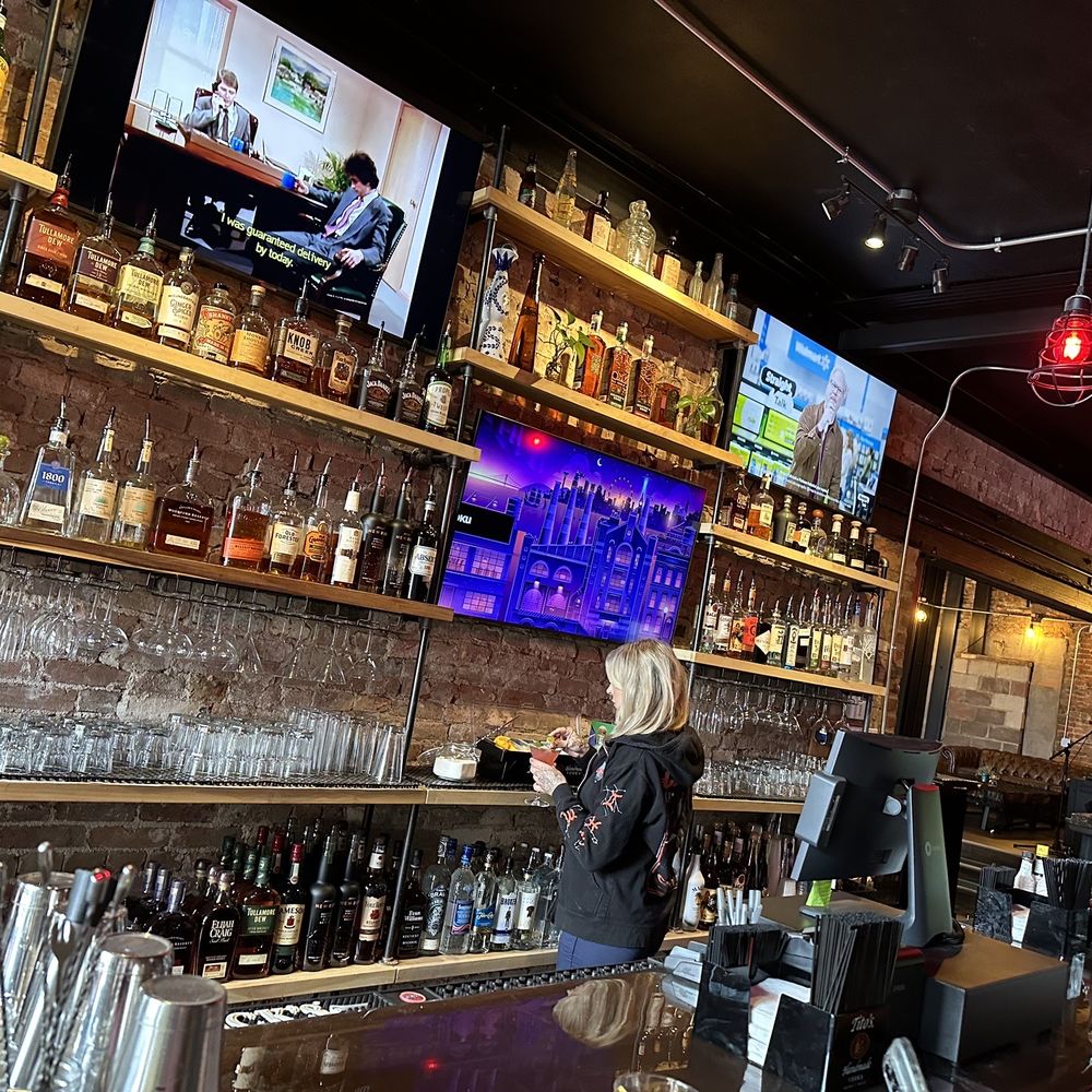 Next Door - a woman at a bar with a television in the background - Beer, Wine & Spirits Near Me - Dayton, Ohio Next Door - a woman at a bar with a television in the background - Beer, Wine & Spirits Near Me - Dayton, Ohio