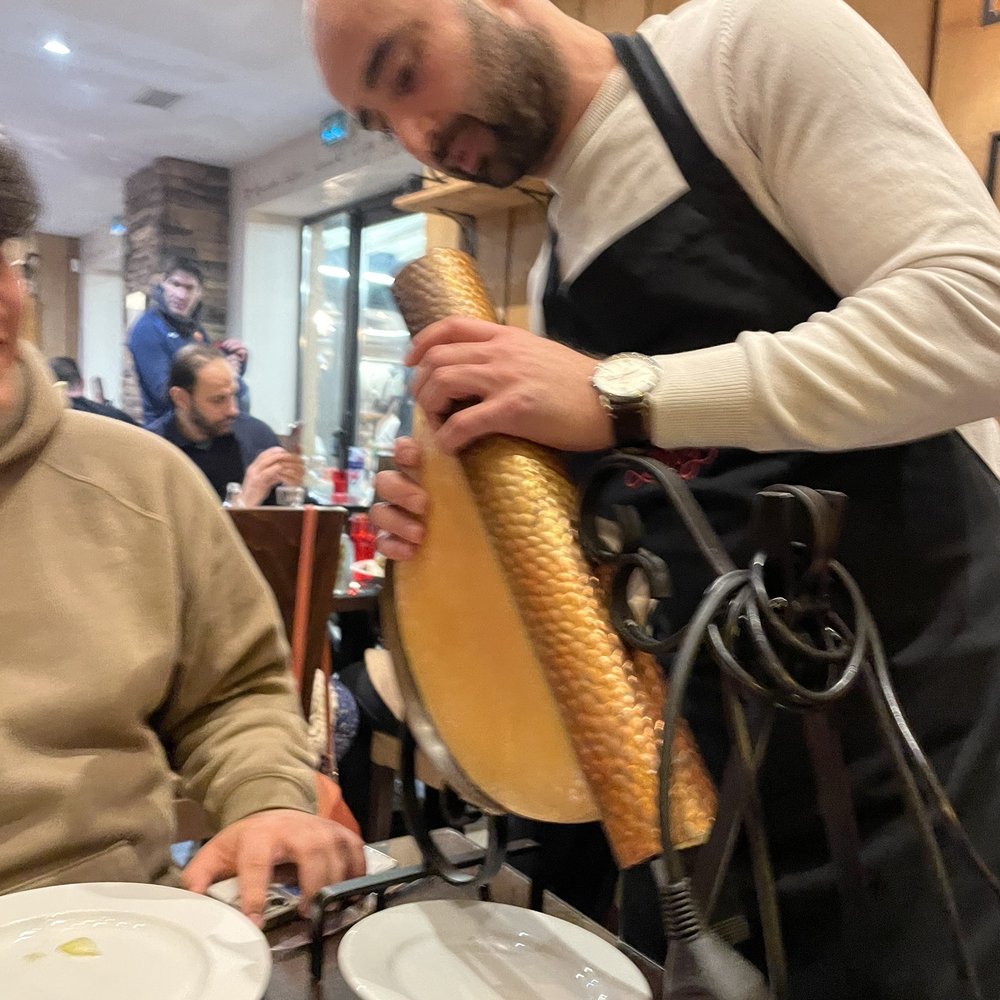 Amir sets up the raclette heater over the giant wheel of cheese.