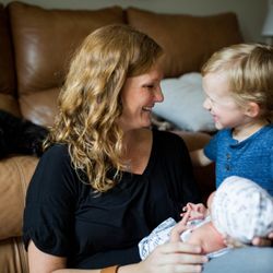 Family Tree Doula Services - Daytime postpartum doula sitting on floor, holding newborn while talking to toddler while parents rest.