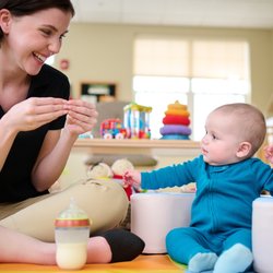 Primrose School at Highlands Ranch Business Park - Primrose Schools infant teacher doing interactive play with baby on colorful floor mat in childcare classroom