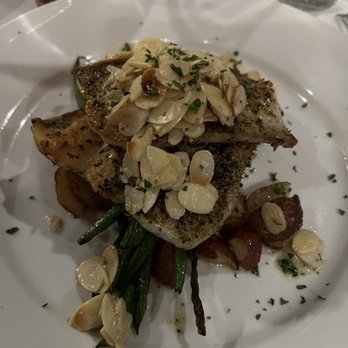Cafe Lynn - A fish fillet garnished with sliced almonds and herbs, served on a white plate with green beans and roasted potatoes in the background. - Seafood Near Me - Mandeville, Louisiana
