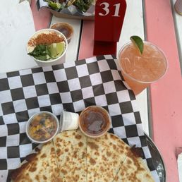 Carne Asada Tacos - A table setting with quesadillas, tacos, a cocktail with lime, and various sauces, with a red table number 31, at a restaurant.