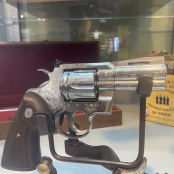 Tombstone Tactical - A silver revolver with engraved patterns is mounted on a stand inside a store, with glass display cases and business signage in the background. - Guns & Ammo Near Me - Phoenix, Arizona