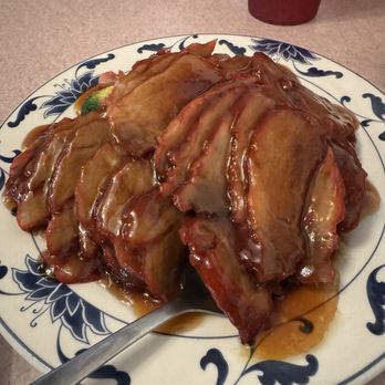 China Garden - Hong Kong BBQ Pork - Sliced barbecue pork with sauce served on a decorative ceramic plate, with a spoon and a red drink in the background. - Chinese Near Me - Bryan, Ohio