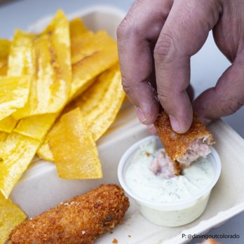 Bodega Cuban Kitchen - a hand dipping a piece of fish - Food Trucks Near Me - Denver, Colorado