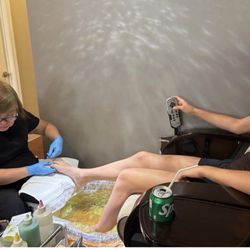 Nail tech watching a show on her phone while doing a pedicure