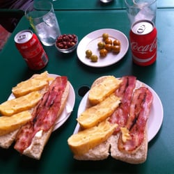 L'Encontre - Almuercito: Bocadillos de tortilla de patata con bacon y ajo aceite acompañado de aceitunas y cacaos de la casa con refresco.