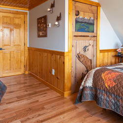 The Inn at Oxbow Acres - Room with a queen bed and a twin bed with wooden floors and a door carved with a fish.