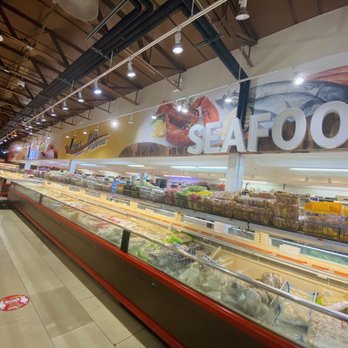 Jmart - Frozen food - Supermarket aisle with frozen seafood and grocery products, with a large 'SEAFOOD' sign overhead and bright lighting. - International Grocery Near Me - Brooklyn, New York