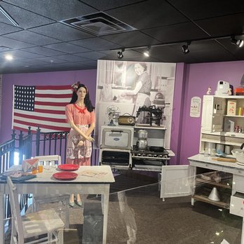 Behringer-Crawford Museum - A museum exhibit features a mannequin in vintage clothing, a retro kitchen setup with old appliances, and an American flag on a purple wall. - Museums Near Me - Covington, Kentucky