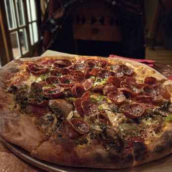 Hawt pizza - Norteno pie - A pizza topped with pepperoni, mushrooms, and green peppers is placed on a metal tray on a wooden table in a restaurant setting. - Pizza Near Me - Santa Fe, New Mexico