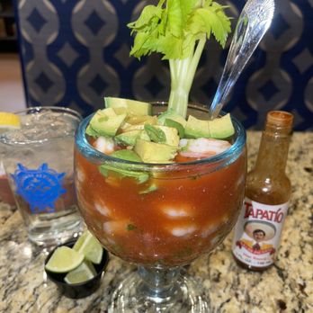 Mariscos Altamar - Seafood cocktail with shrimp, avocado, and celery in a large glass, accompanied by lime wedges and hot sauce, on a granite table. - Seafood Near Me - Los Lunas, New Mexico