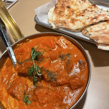 Spice Room - Sweet Potato Masala - A bowl of chicken curry with a rich, orange sauce and garnished with herbs, accompanied by naan bread on a tray. - Indian Near Me - Arvada, Colorado