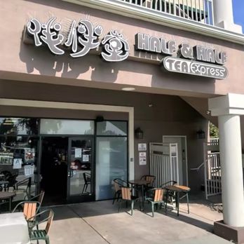 Half and Half Tea Express - Storefront - The image depicts the storefront of Half & Half Tea Express in Pasadena, California. The building features a beige facade with white columns supporting an overhang. The signage includes Chinese characters and the business name in English, along with a tea-themed logo. Outdoor seating with tables and chairs is arranged in front of the entrance, and a staircase on the right side leads to an upper level. The scene is set during daylight with clear weather, and some greenery is visible on the right side. - Coffee & Tea Near Me - Pasadena, California