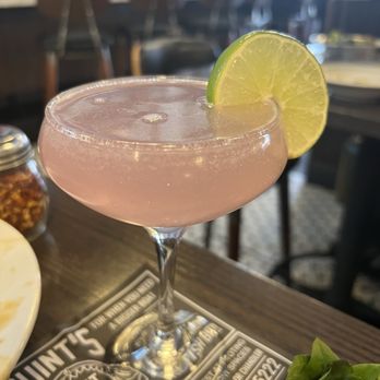 Bettola - Lavender cocktail - A pink cocktail in a coupe glass garnished with a lime slice, placed on a bar table with a menu underneath. - Pizza Near Me - Cranston, Rhode Island