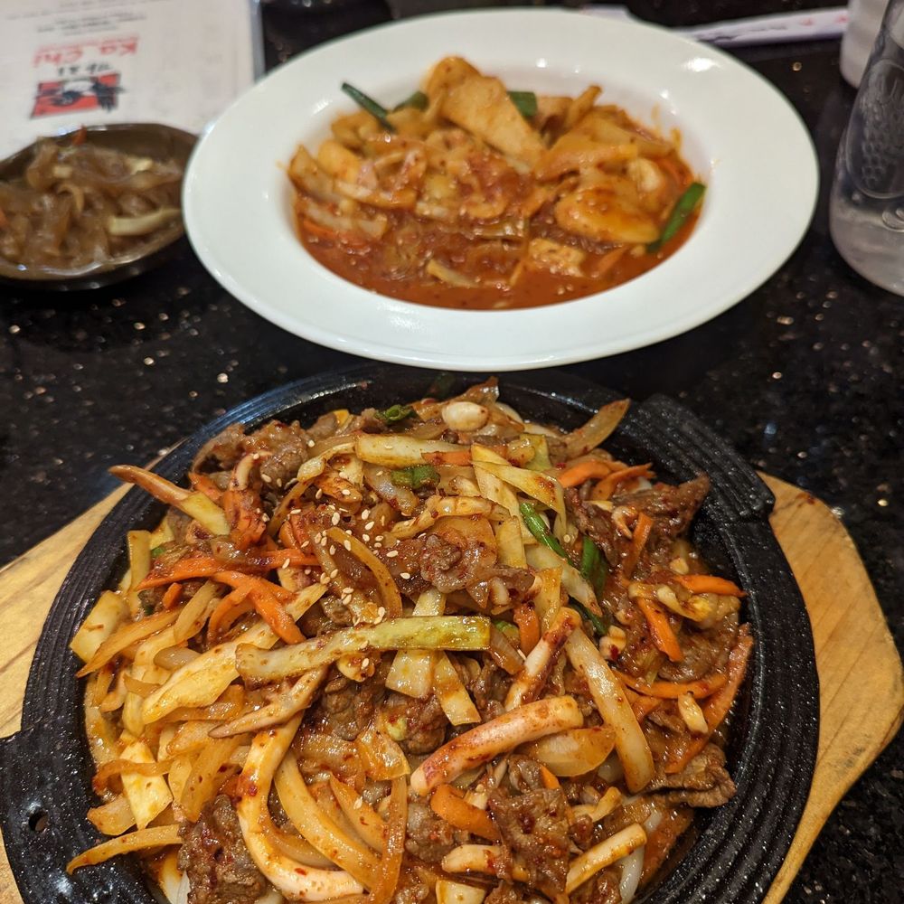 Spicy stir fried udon with squid + beef at the front and dukbokki in the back Spicy stir fried udon with squid + beef at the front and dukbokki in the back