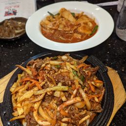 Spicy stir fried udon with squid + beef at the front and dukbokki in the back Spicy stir fried udon with squid + beef at the front and dukbokki in the back
