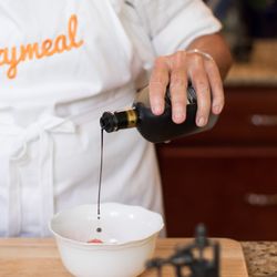 Mixing balsamic vinegar with olive oil and rosemary to coat fresh grapes before roasting.
