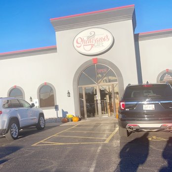 Shawano’s Cafe - Entrance - Shawano's Cafe storefront in Shawano, WI, features an arched entrance, a sign, and a parking lot with several cars under a blue sky. - Seafood Near Me - Shawano, Wisconsin