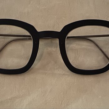 Eyeglass Express - A pair of black eyeglasses with a thick, rounded frame and clear lenses are positioned on a light-colored surface. The glasses have metal temples that extend from the frame, with transparent tips. The image focuses on the glasses, showing their design and construction clearly. - Eyewear & Opticians Near Me - Temecula, California