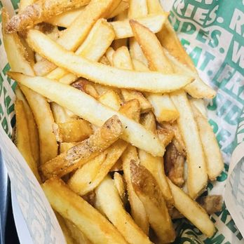 Wingstop - A basket filled with French fries, served in a paper liner with green text, appears to be from a fast-food restaurant. The fries are golden-brown, with some slightly darker edges, and are cut in a typical style. The basket is placed on a black tray, with a red object partially visible in the background. - Chicken Wings Near Me - Laurel, Maryland