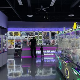 Claw machine counter with upgrade plushies behind it, and claw machine arcades on the sides.