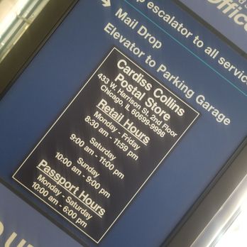 US Post Office - The image features a digital display board at a US Post Office, providing directions to various services such as the elevator, mail drop, and parking garage. It also lists the hours of operation for the Carlas Collins Postal Store and passport services, including specific opening and closing times for each day of the week. The display is angled and set against a background that suggests an indoor postal facility. - Post Offices Near Me - Chicago, Illinois