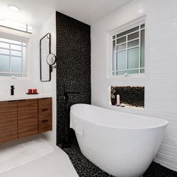 Lumina Builders - Elegant bathroom featuring dark wood cabinets with white countertops, dark flooring, and white walls.