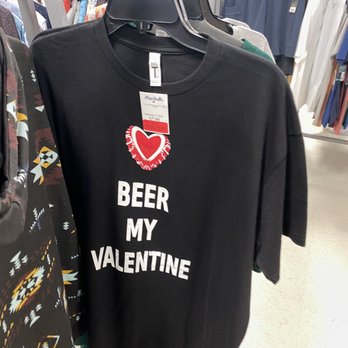 Marshalls - A black T-shirt with white text "BEER MY VALENTINE" and a red heart graphic is displayed on a hanger in a retail store, surrounded by other clothing items. - Department Stores Near Me - Boynton Beach, Florida