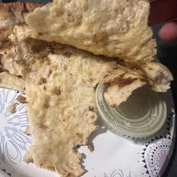 Where's the filling? - A piece of naan bread is held above a decorative plate with a small container of sauce, likely served at a restaurant.
