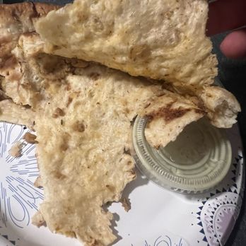 Dera - Where's the filling? - A piece of naan bread is held above a decorative plate with a small container of sauce, likely served at a restaurant. - Pakistani Near Me - Springfield, Virginia
