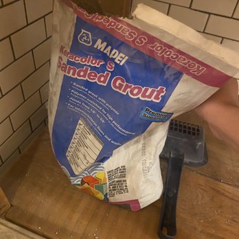 Out-U-Go! - Literally says Sanded Grout in huge letters on the bag... - A bag of Keracolor S Sanded Grout with a trowel resting on a wooden surface near a brick wall. - Dog Walkers Near Me - Chicago, Illinois