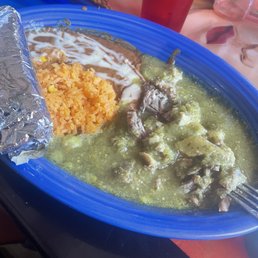 Not much pork under there! - A blue plate contains Mexican cuisine including rice, meat in green sauce, beans with sour cream, and a foil-wrapped item.