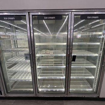 CVS Pharmacy - Ice cream for 999 happy haunts - A glass-fronted refrigerated display case with three sections, each labeled 'ice cream,' is shown with empty wire shelves inside. The case is situated indoors, likely in a retail or grocery store, with reflections of store lighting visible on the glass doors. - Drugstores Near Me - Burbank, California