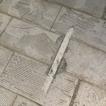 Costa's Masonry - a close up of a tile floor - The image shows a tiled floor with a damaged tile and a metal tool placed on it, possibly during a repair or construction process. - Stonemasons Near Me - Methuen, Massachusetts