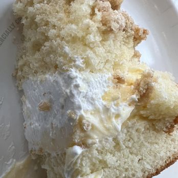 King Kullen - a piece of cake on a plate - A close-up of a vanilla cake slice with white frosting, cream filling, and cake crumbs on top, served on a white plate. - Grocery Near Me - Wading River, New York