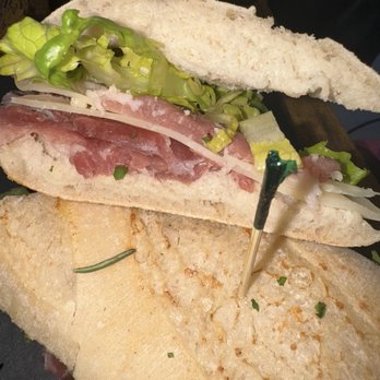 Arre - Prosciutto sandwich - A sandwich with prosciutto, lettuce, and cheese on white bread, accompanied by a breaded cutlet, served on a dark plate. - Bakeries Near Me - Miami, Florida